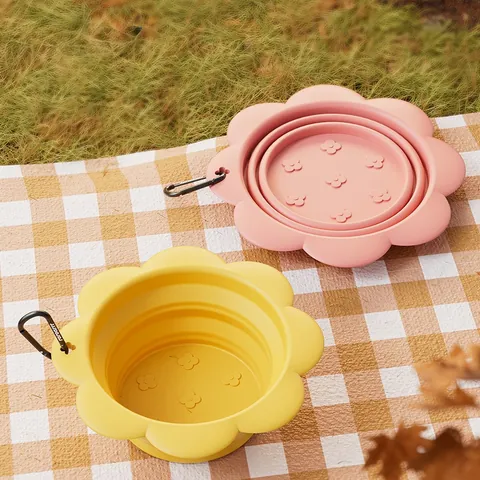 Yellow and pink flower-shaped collapsible silicone bowls with carabiners on a check picnic blanket